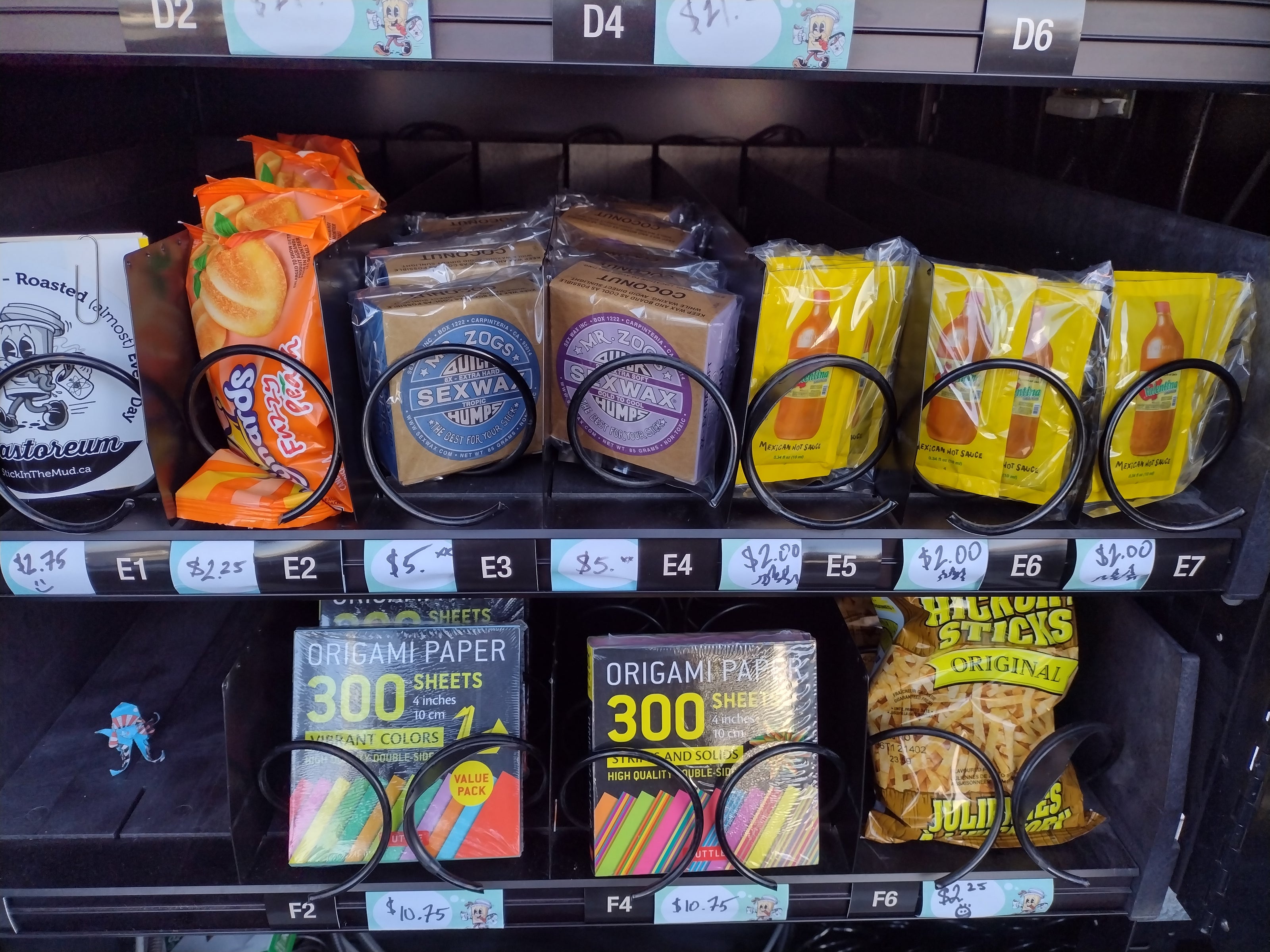 items inside of vending machine coils including Maynards Fuzzy Peaches, Mr. Zogs Sex Wax for surf boards, Valentina's hot sauce packets, and Tuttle Origami paper.